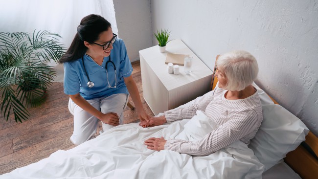 A nurse sits at a patient’s bedside.