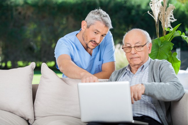 A nurse assists an older adult patient on a laptop.