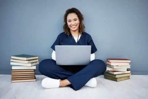 Rockhurst Online nursing student studying for NCLEX exam at laptop next to textbooks